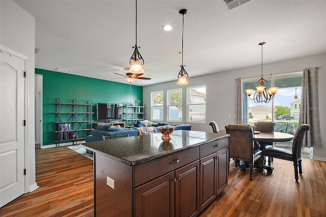 kitchen with decorative light fixtures, dark wood-type flooring, visible vents, and ceiling fan with notable chandelier