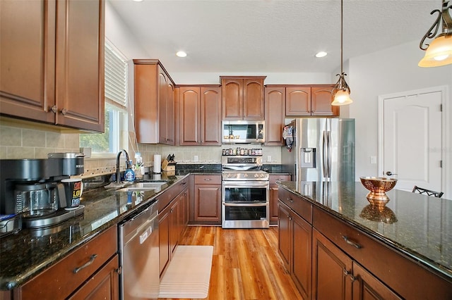 kitchen with decorative backsplash, a sink, appliances with stainless steel finishes, light wood-style floors, and hanging light fixtures