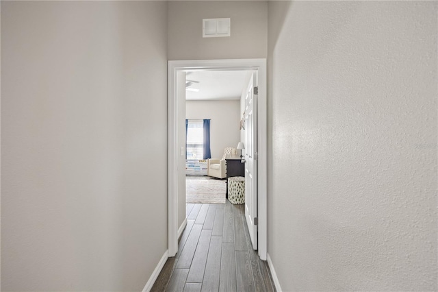 hallway with visible vents, a textured wall, dark wood-style flooring, and baseboards