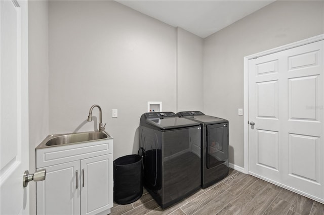 washroom featuring cabinet space, a sink, independent washer and dryer, light wood-style flooring, and baseboards