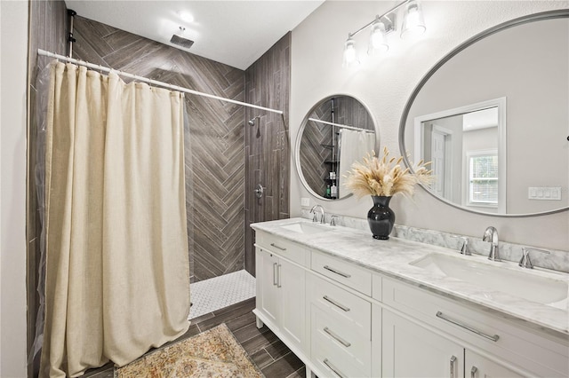 bathroom with wood finish floors, a tile shower, double vanity, and a sink