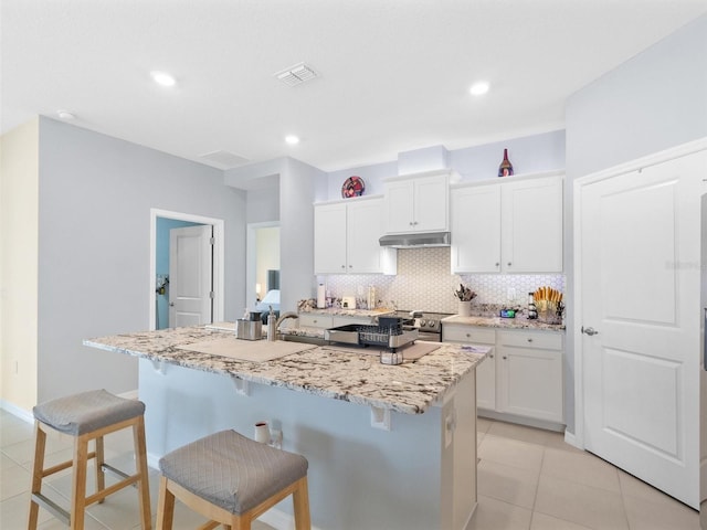 kitchen featuring a breakfast bar, white cabinets, backsplash, and under cabinet range hood
