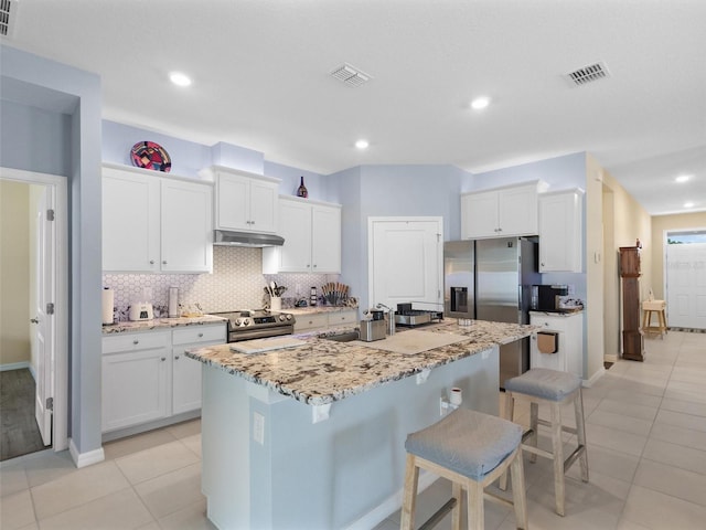 kitchen with light tile patterned floors, decorative backsplash, appliances with stainless steel finishes, a breakfast bar, and visible vents