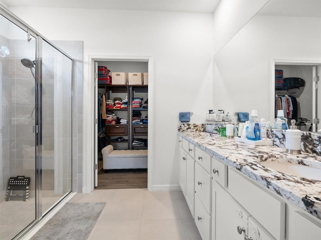 bathroom with a walk in closet, baseboards, a shower stall, and double vanity