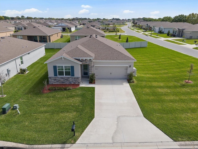 view of front of house featuring a residential view, stone siding, a front yard, concrete driveway, and an attached garage