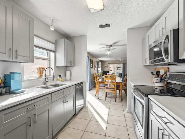 kitchen featuring ceiling fan, light countertops, gray cabinets, a sink, and appliances with stainless steel finishes