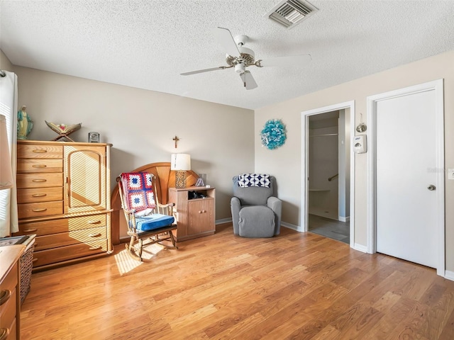 living area with light wood-style floors, ceiling fan, a textured ceiling, and visible vents