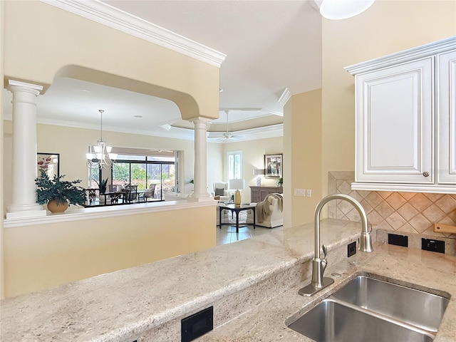 1842 Lake Ridge Dr, The Villages, FL 32162 - kitchen featuring crown molding, light stone counters, a sink, decorative columns, and tasteful backsplash