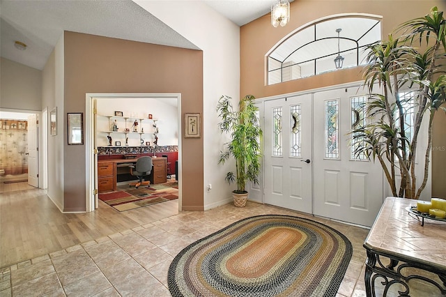 entryway featuring baseboards, light tile patterned floors, and a towering ceiling