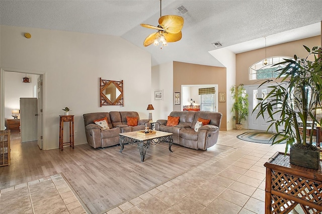 living area with light tile patterned floors, high vaulted ceiling, ceiling fan, and visible vents