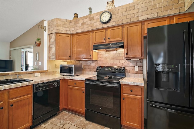kitchen featuring tasteful backsplash, black appliances, lofted ceiling, tile counters, and under cabinet range hood