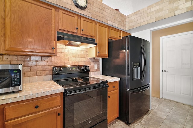 kitchen with backsplash, black appliances, tile counters, under cabinet range hood, and light tile patterned flooring