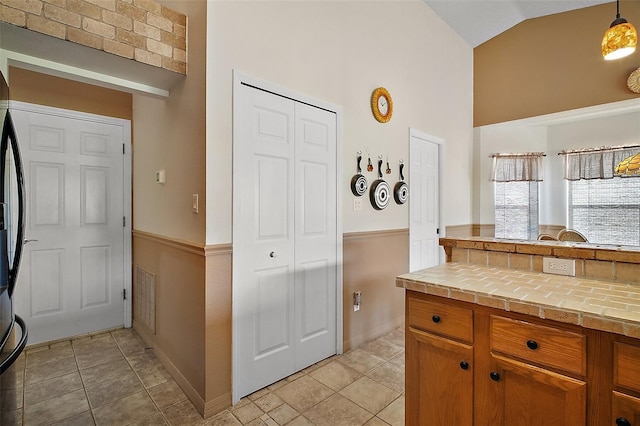 kitchen featuring brown cabinets, high vaulted ceiling, tile countertops, baseboards, and visible vents