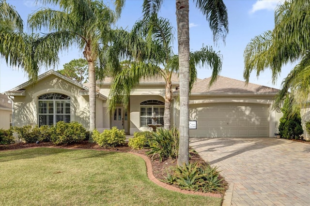 mediterranean / spanish-style house featuring a garage, stucco siding, decorative driveway, and a front yard