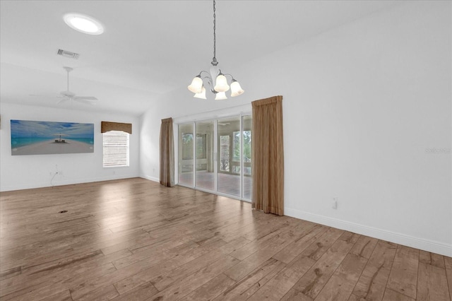unfurnished dining area featuring visible vents, vaulted ceiling, baseboards, wood finished floors, and ceiling fan with notable chandelier