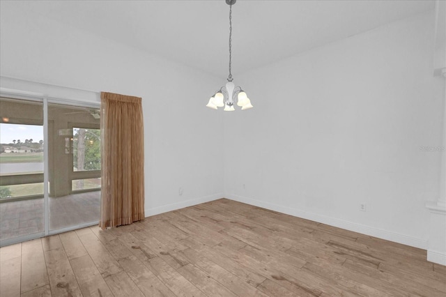 spare room featuring a chandelier, wood finished floors, and baseboards