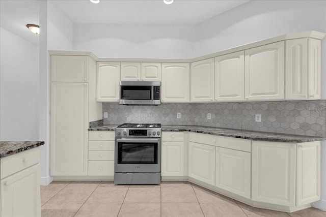 kitchen with dark stone counters, stainless steel appliances, tasteful backsplash, and light tile patterned floors