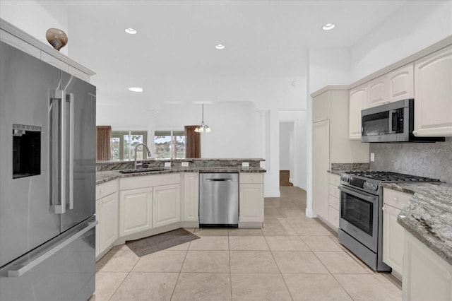 kitchen featuring a sink, stainless steel appliances, tasteful backsplash, a peninsula, and stone countertops