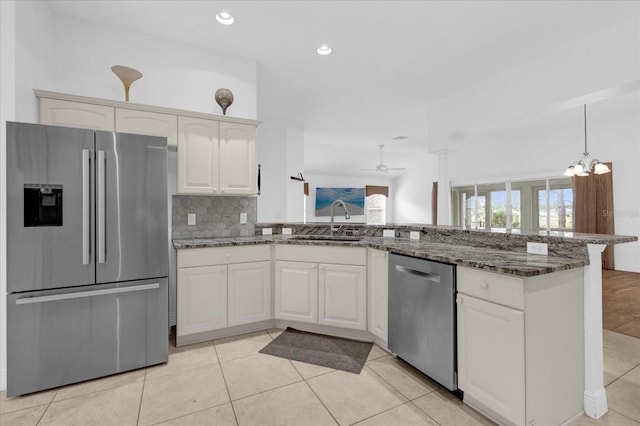 kitchen featuring dark stone counters, appliances with stainless steel finishes, a sink, a ceiling fan, and a peninsula