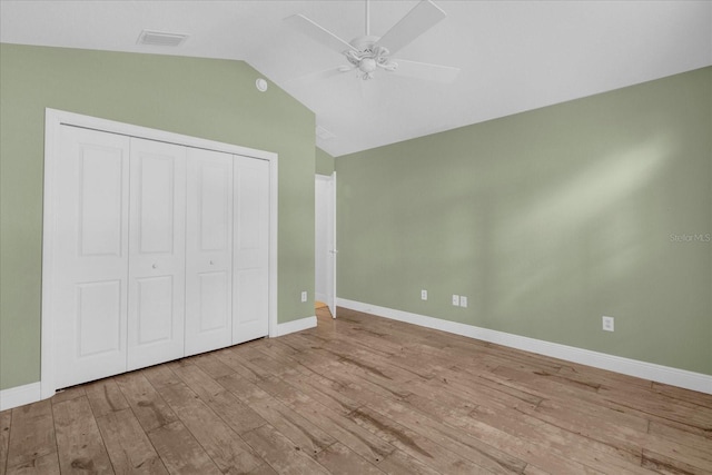 unfurnished bedroom with a closet, visible vents, vaulted ceiling, baseboards, and hardwood / wood-style floors