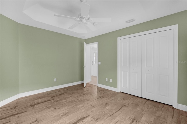 unfurnished bedroom featuring wood finished floors, a closet, ceiling fan, baseboards, and visible vents