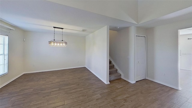 empty room with stairs, visible vents, wood finished floors, and baseboards