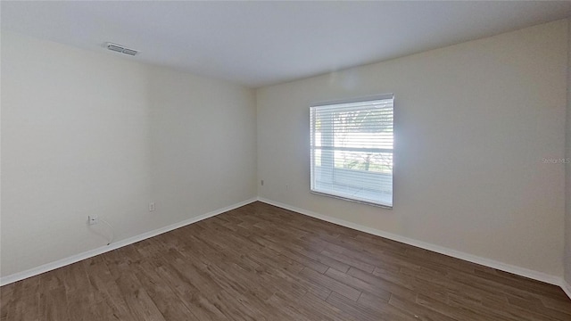unfurnished room featuring dark wood-style floors, visible vents, and baseboards
