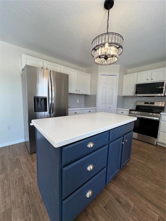 kitchen with appliances with stainless steel finishes, an inviting chandelier, white cabinetry, and blue cabinetry