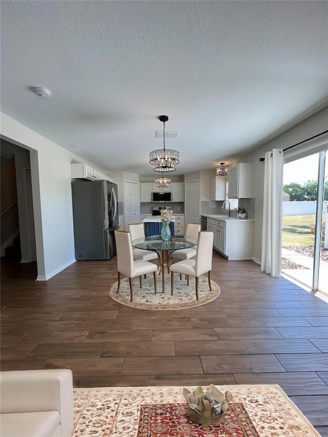 dining room featuring an inviting chandelier, baseboards, visible vents, wood finish floors, and a textured ceiling