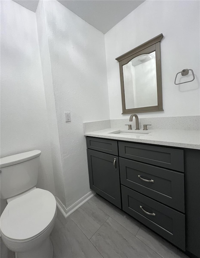 half bath with vanity, toilet, marble finish floor, and baseboards