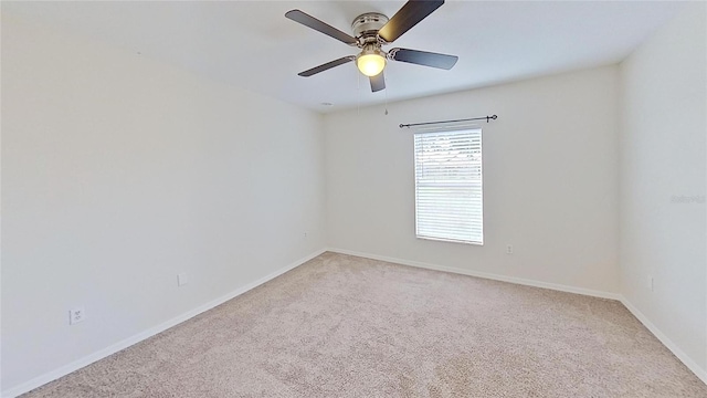 spare room with light colored carpet, a ceiling fan, and baseboards