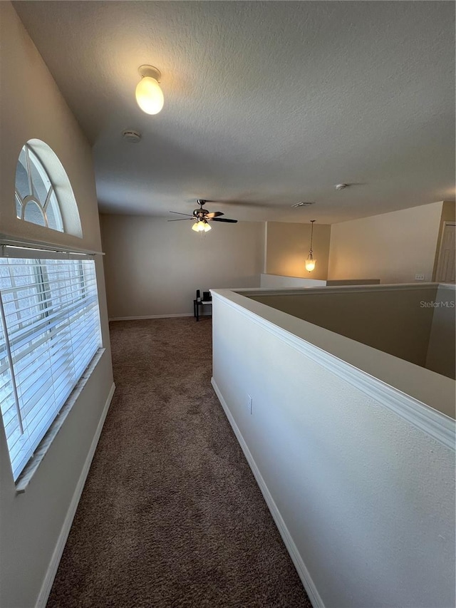 hallway featuring baseboards, dark colored carpet, a textured ceiling, and an upstairs landing
