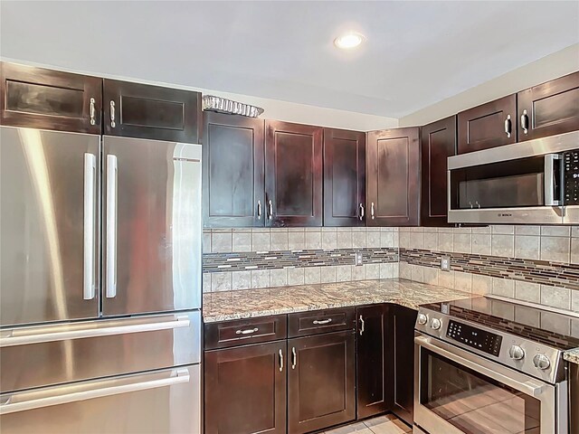 kitchen with light stone countertops, appliances with stainless steel finishes, dark brown cabinetry, and tasteful backsplash