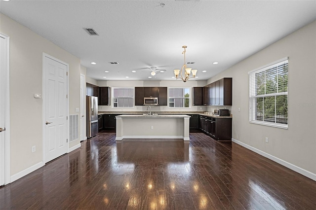 kitchen featuring dark wood-style flooring, dark brown cabinetry, an island with sink, light countertops, and appliances with stainless steel finishes
