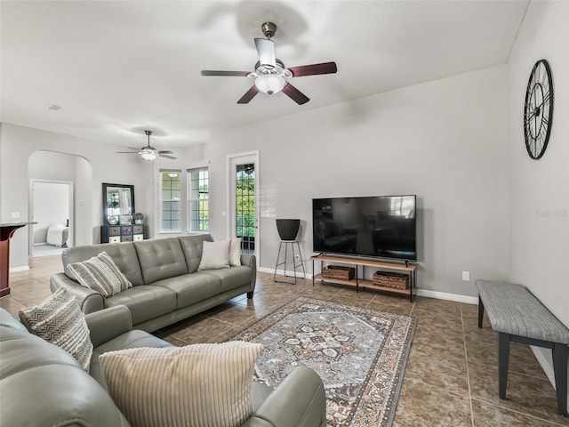 living area with baseboards, a ceiling fan, and arched walkways