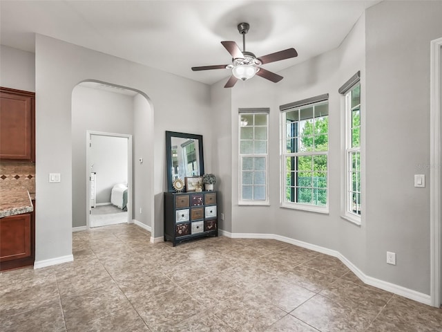 empty room featuring light tile patterned floors, baseboards, a ceiling fan, and arched walkways