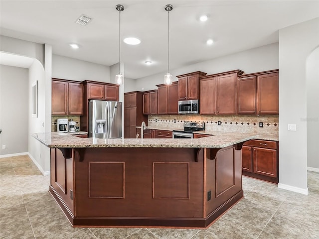 kitchen with tasteful backsplash, a breakfast bar area, light stone countertops, hanging light fixtures, and appliances with stainless steel finishes