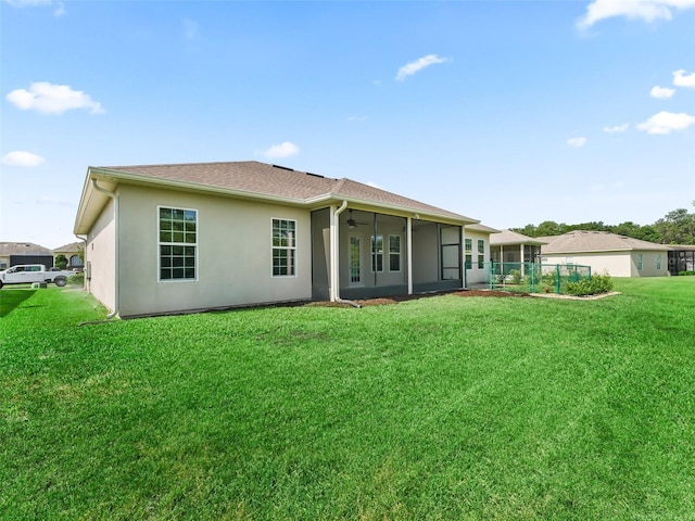 rear view of property featuring a ceiling fan, stucco siding, a sunroom, and a lawn