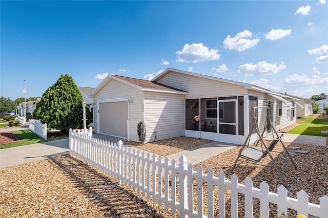 view of front of property featuring an attached garage, a sunroom, concrete driveway, roof with shingles, and fence private yard