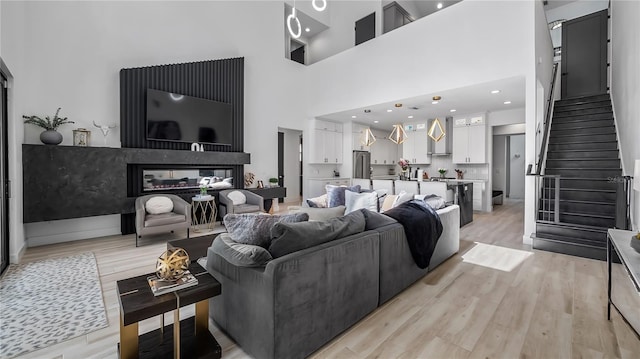 living area featuring a multi sided fireplace, stairway, light wood finished floors, and a towering ceiling