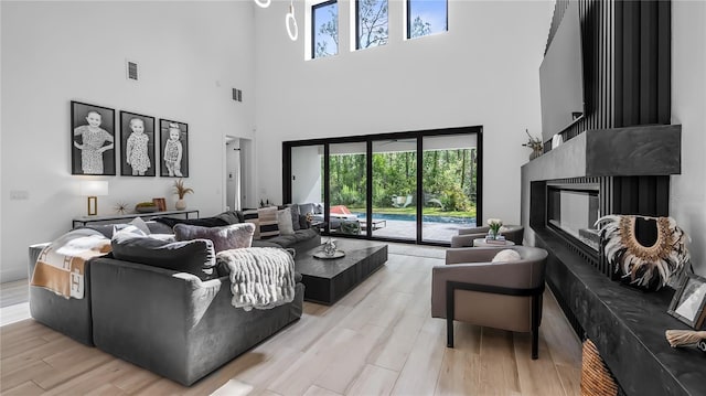 living room with visible vents, a glass covered fireplace, a high ceiling, and a wealth of natural light