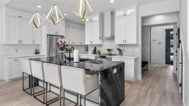 kitchen featuring decorative backsplash, a kitchen breakfast bar, wall chimney range hood, a sink, and appliances with stainless steel finishes