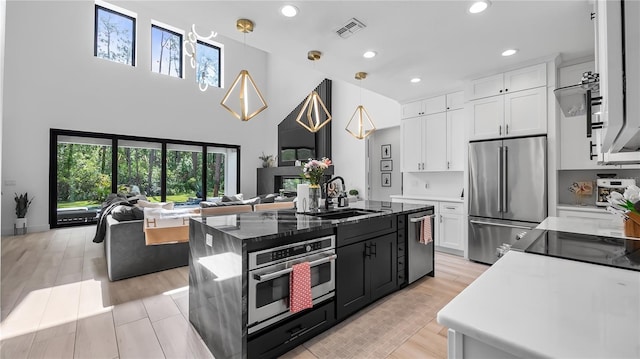 kitchen featuring hanging light fixtures, a sink, white cabinets, open floor plan, and stainless steel appliances