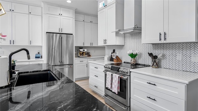 kitchen with a sink, white cabinetry, wall chimney range hood, and stainless steel appliances