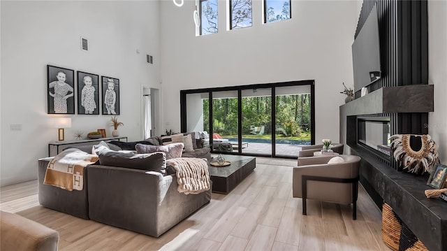 living room featuring visible vents, light wood-style flooring, a high ceiling, and a fireplace
