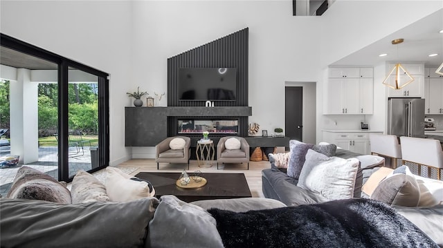 living room featuring a high ceiling, a glass covered fireplace, and light wood-type flooring