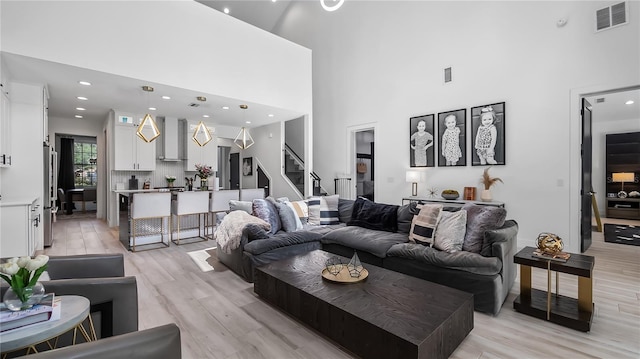 living area with stairway, a high ceiling, light wood finished floors, and visible vents