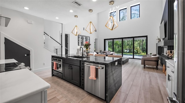 kitchen with a sink, a kitchen island with sink, stainless steel appliances, open floor plan, and visible vents