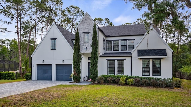 modern farmhouse featuring a garage, a front yard, decorative driveway, roof with shingles, and stucco siding