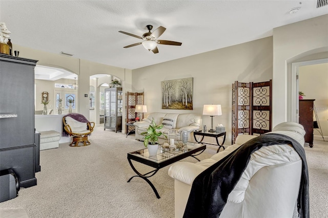 living room featuring arched walkways, a ceiling fan, visible vents, and carpet